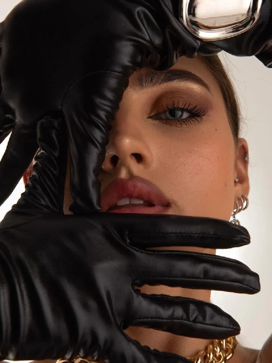 Русский промпт: Photo of a woman with fair skin and blue eyes, wearing black leather gloves and a gold chain choker. She has a serious expression and is looking directly at the camera. The background is a plain white wall. The lighting is soft and natural, highlighting her features. The image is a close-up shot, focusing on her face and hands. | Original prompt: Photo of a woman with fair skin and blue eyes, wearing black leather gloves and a gold chain choker. She has a serious expression and is looking directly at the camera. The background is a plain white wall. The lighting is soft and natural, highlighting her features. The image is a close-up shot, focusing on her face and hands.