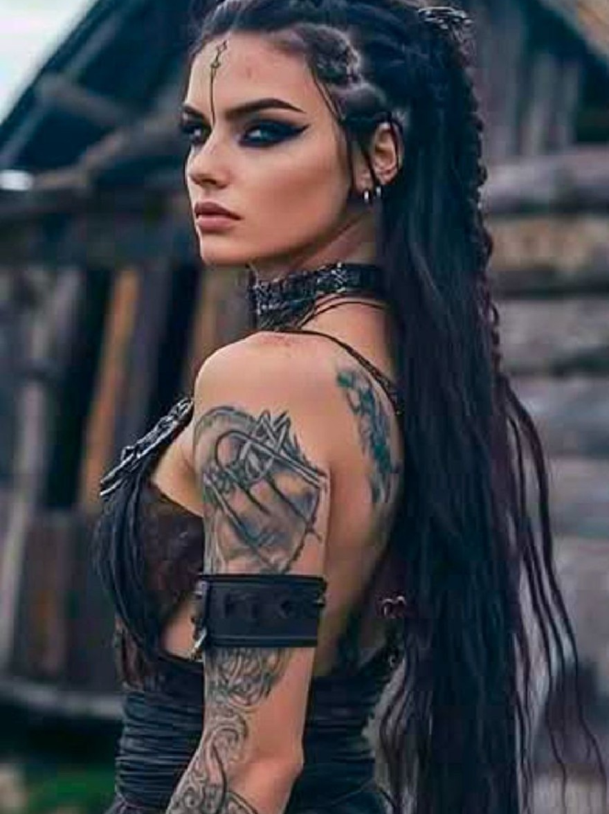 Русский промпт: Женщина с длинными темными волосами, приготовленными в косу, в черном кофе и черном кожаном наряде. У нее серьезное выражение и стоит перед деревенским деревянным домом. Ее рука украшена сложными татуировками. Освещение мягкое и естественное, подчеркивая ее темную кожу и замысловатые узоры на ее руках. Фон размыта, подчеркивая женщину и ее татуировки. | Original prompt: A woman with long, dark hair styled in a braid, wearing a black choker and a black leather outfit. She has a serious expression and is standing in front of a rustic wooden house. Her arm is adorned with intricate tattoos. The lighting is soft and natural, highlighting her dark skin and the intricate designs on her arms. The background is blurred, emphasizing the woman and her tattoos.