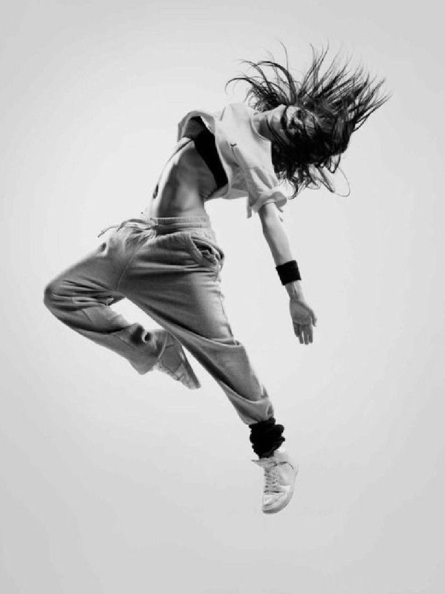 Русский промпт: Черно -белая фотография молодой женщины, прыгающей в воздухе, с ее волосами дули на ветру. На ней укороченная белая футболка и подходящие спортивные штаны, в сочетании с белыми кроссовками. Ее руки растянуты по бокам, и у нее на лице решительное выражение. Фон прост и минималистичен, без других объектов или людей в кадре. Освещение мягкое и равномерное, подчеркивая ее изящные движения. Общее настроение энергично и динамично. | Original prompt: A black and white photograph of a young woman jumping in the air with her hair blowing in the wind. She is wearing a cropped white t-shirt and matching sweatpants, paired with white sneakers. Her arms are stretched out to the sides, and she has a determined expression on her face. The background is plain and minimalistic, with no other objects or people in the frame. The lighting is soft and even, highlighting her graceful movements. The overall mood is energetic and dynamic.