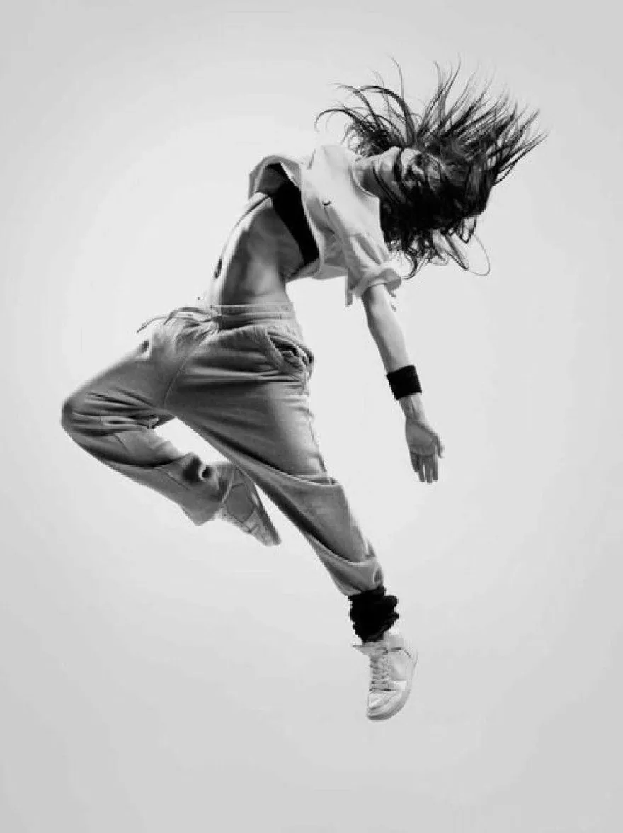 Русский промпт: Черно -белая фотография молодой женщины, прыгающей в воздухе, с ее волосами дули на ветру. На ней укороченная белая футболка и подходящие спортивные штаны, в сочетании с белыми кроссовками. Ее руки растянуты по бокам, и у нее на лице решительное выражение. Фон прост и минималистичен, без других объектов или людей в кадре. Освещение мягкое и равномерное, подчеркивая ее изящные движения. Общее настроение энергично и динамично. | Original prompt: A black and white photograph of a young woman jumping in the air with her hair blowing in the wind. She is wearing a cropped white t-shirt and matching sweatpants, paired with white sneakers. Her arms are stretched out to the sides, and she has a determined expression on her face. The background is plain and minimalistic, with no other objects or people in the frame. The lighting is soft and even, highlighting her graceful movements. The overall mood is energetic and dynamic.