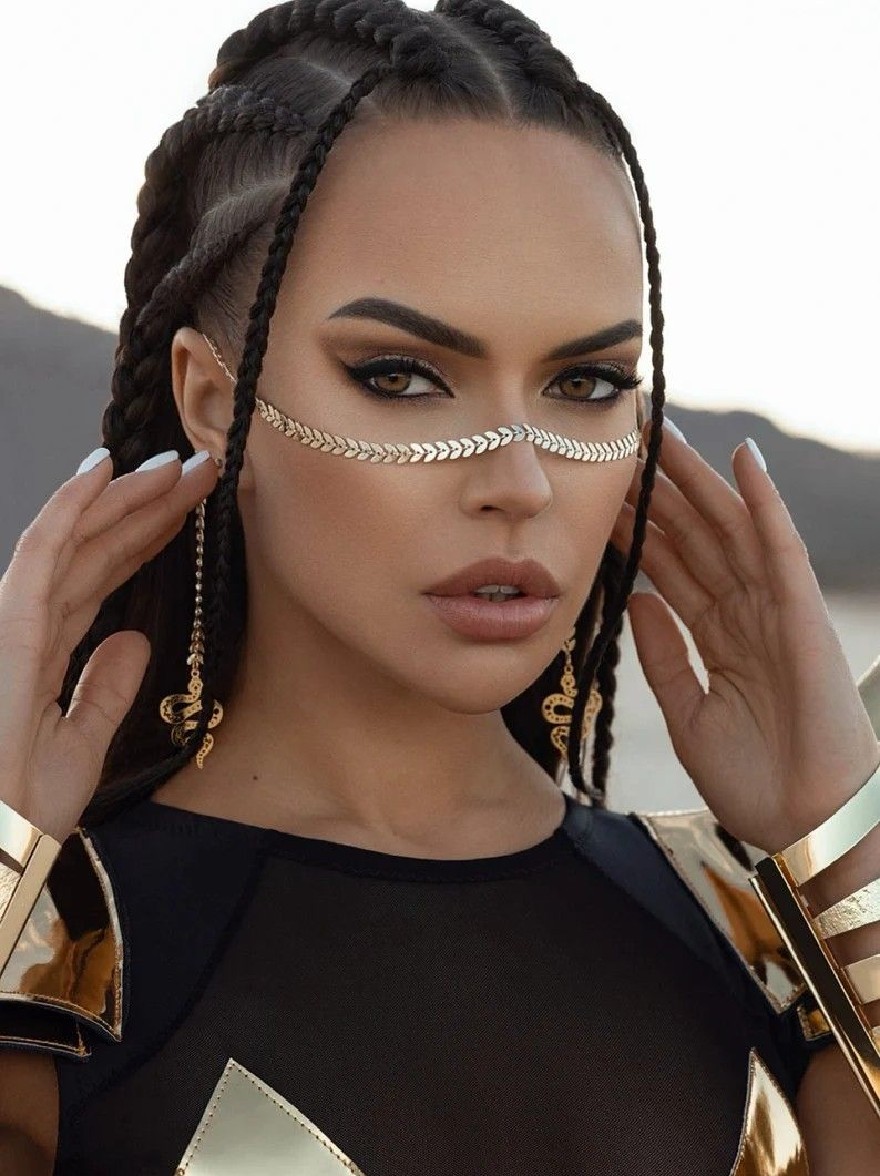 Русский промпт: Фотография красивой афро-американской женщины с длинными плетеными волосами, одетая в черный и золотой наряд с геометрическим дизайном. У нее серьезное выражение, и она держит волосы обеими руками. Фон размыт, но, похоже, это наружная обстановка с горами на расстоянии. Освещение мягкое и естественное, подчеркивая ее черты. Изображение высокое качество и имеет профессиональное чувство. | Original prompt: Photo of a beautiful African-American woman with long braided hair, wearing a black and gold outfit with a geometric design. She has a serious expression and is holding her hair with both hands. The background is blurred, but it appears to be an outdoor setting with mountains in the distance. The lighting is soft and natural, highlighting her features. The image is high quality and has a professional feel.