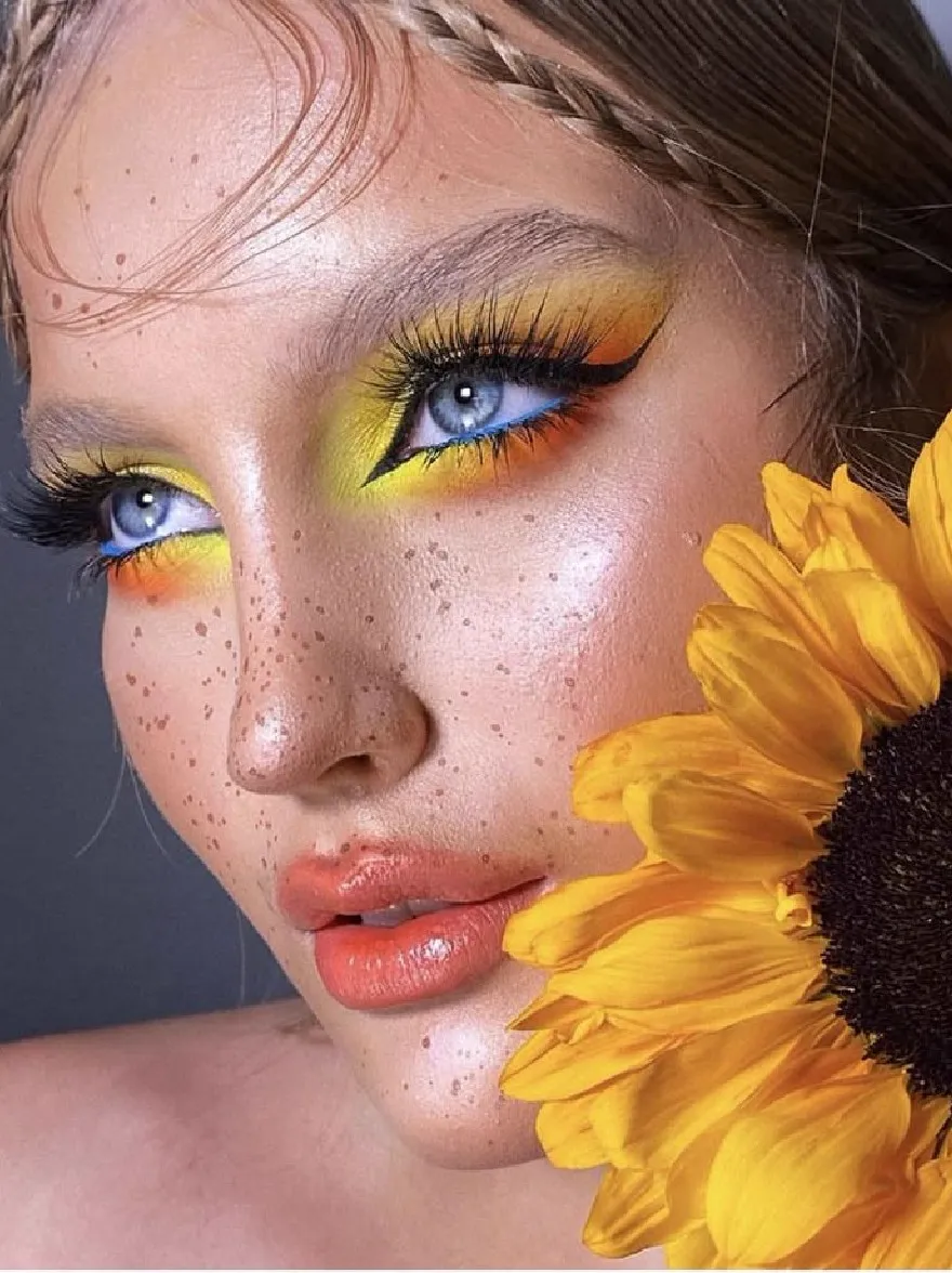 Русский промпт: A close-up photograph of a young woman with fair skin and blue eyes, adorned with bright yellow and orange eye makeup. She has long, braided blonde hair and is holding a large, sunflower in her right hand. Her lips are painted a vibrant orange, and she has a subtle, freckled texture on her face. The background is a simple, dark grey. The lighting is soft and natural, highlighting her face and the flower. The image has a dreamy, ethereal quality. | Original prompt: A close-up photograph of a young woman with fair skin and blue eyes, adorned with bright yellow and orange eye makeup. She has long, braided blonde hair and is holding a large, sunflower in her right hand. Her lips are painted a vibrant orange, and she has a subtle, freckled texture on her face. The background is a simple, dark grey. The lighting is soft and natural, highlighting her face and the flower. The image has a dreamy, ethereal quality.