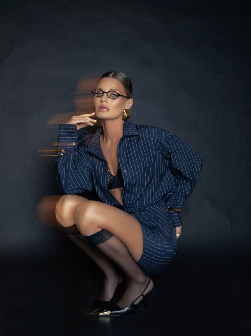Русский промпт: Photo of a woman with dark skin, wearing a navy blue pinstripe suit with gold accents, black thigh-high stockings, and black high heels. She has short, dark hair styled in a sleek, straight look. She is squatting down with her hands resting on her knees, looking directly at the camera with a serious expression. The background is a dark, textured wall. The lighting is dramatic, casting a soft glow on her face and body. The overall mood is sophisticated and edgy. | Original prompt: Photo of a woman with dark skin, wearing a navy blue pinstripe suit with gold accents, black thigh-high stockings, and black high heels. She has short, dark hair styled in a sleek, straight look. She is squatting down with her hands resting on her knees, looking directly at the camera with a serious expression. The background is a dark, textured wall. The lighting is dramatic, casting a soft glow on her face and body. The overall mood is sophisticated and edgy.