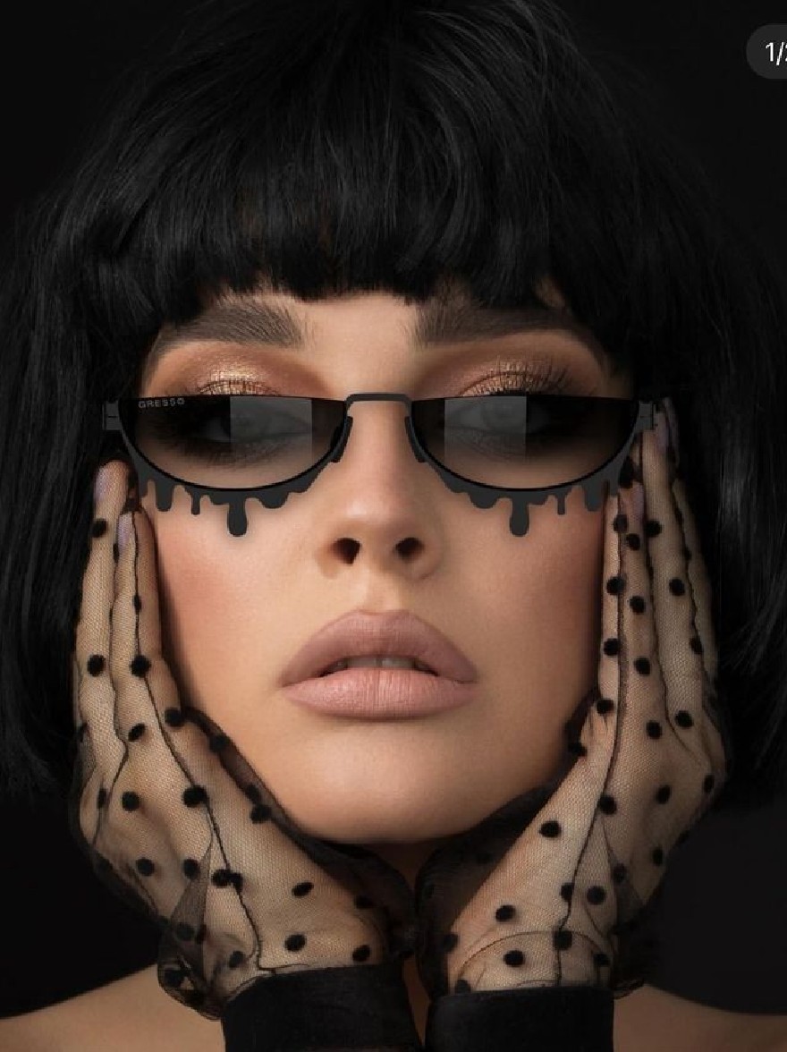 Русский промпт: A close-up photograph of a young woman with a short, blunt black bob haircut and a serious expression. She is wearing black sunglasses with black drips of black paint on them, and sheer, black polka-dot gloves covering her hands. The background is a solid black color. The lighting is dramatic, highlighting her face and the glasses. The image has a minimalistic, artistic style with a focus on the woman's face and sunglasses. The overall mood is sophisticated and edgy. | Original prompt: A close-up photograph of a young woman with a short, blunt black bob haircut and a serious expression. She is wearing black sunglasses with black drips of black paint on them, and sheer, black polka-dot gloves covering her hands. The background is a solid black color. The lighting is dramatic, highlighting her face and the glasses. The image has a minimalistic, artistic style with a focus on the woman's face and sunglasses. The overall mood is sophisticated and edgy.